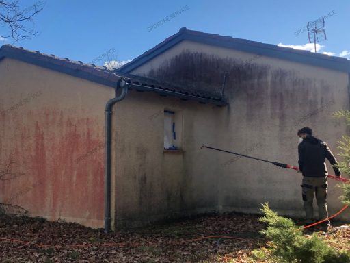 Nettoyage d'une façade de maison Un homme nettoie un mur extérieur avec un nettoyeur haute pression.