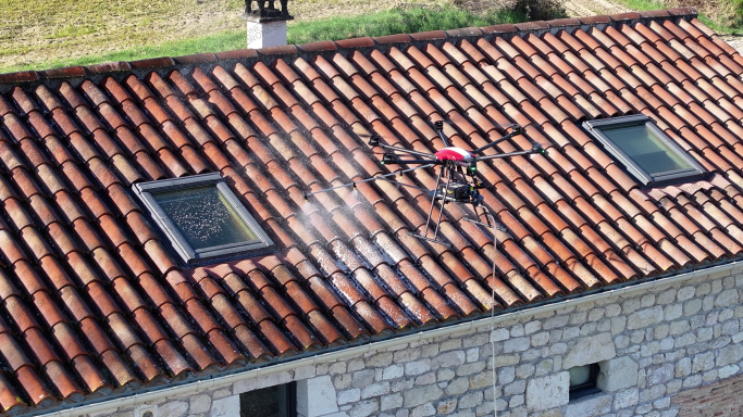 Pulvérisation anti-mousses par drone Drone survole un toit en tuiles, pulvérisant un produit sur la surface.